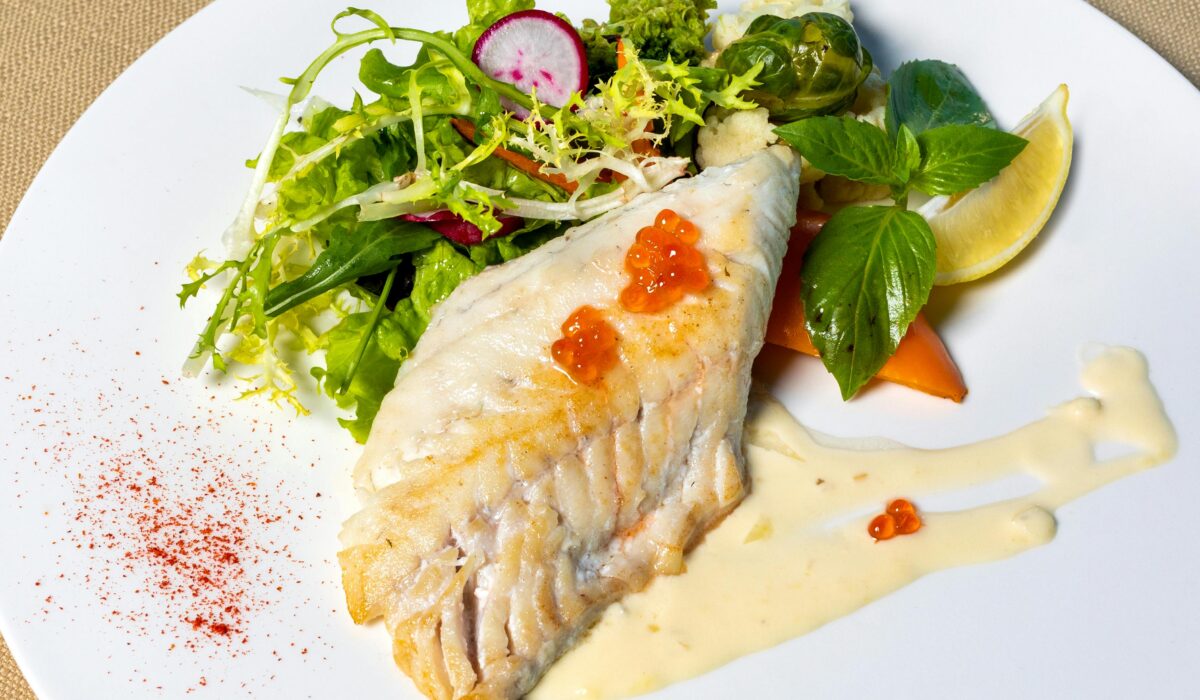 Delicious grilled fish fillet served with fresh mixed greens and sauce on a plate.